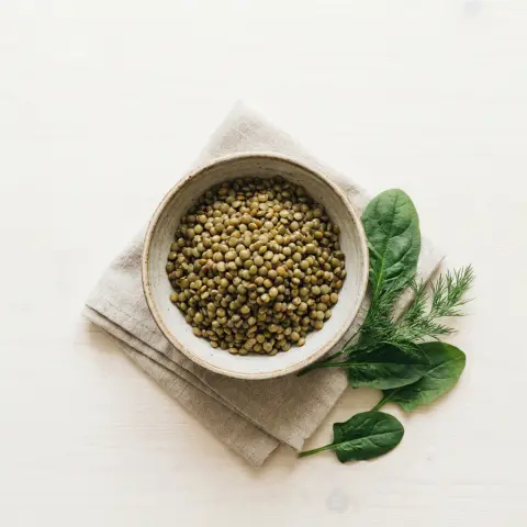 Keten peçete üzerindeki seramik kasede yeşil mercimek, yanında ıspanak ve dereotu